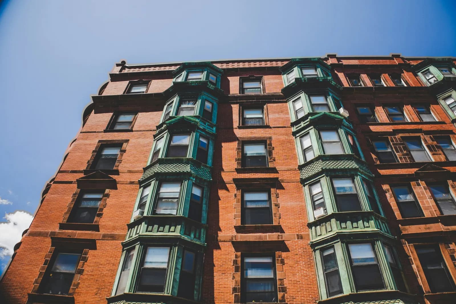 A brick Boston apartment building with copper bay windows, seen from below.