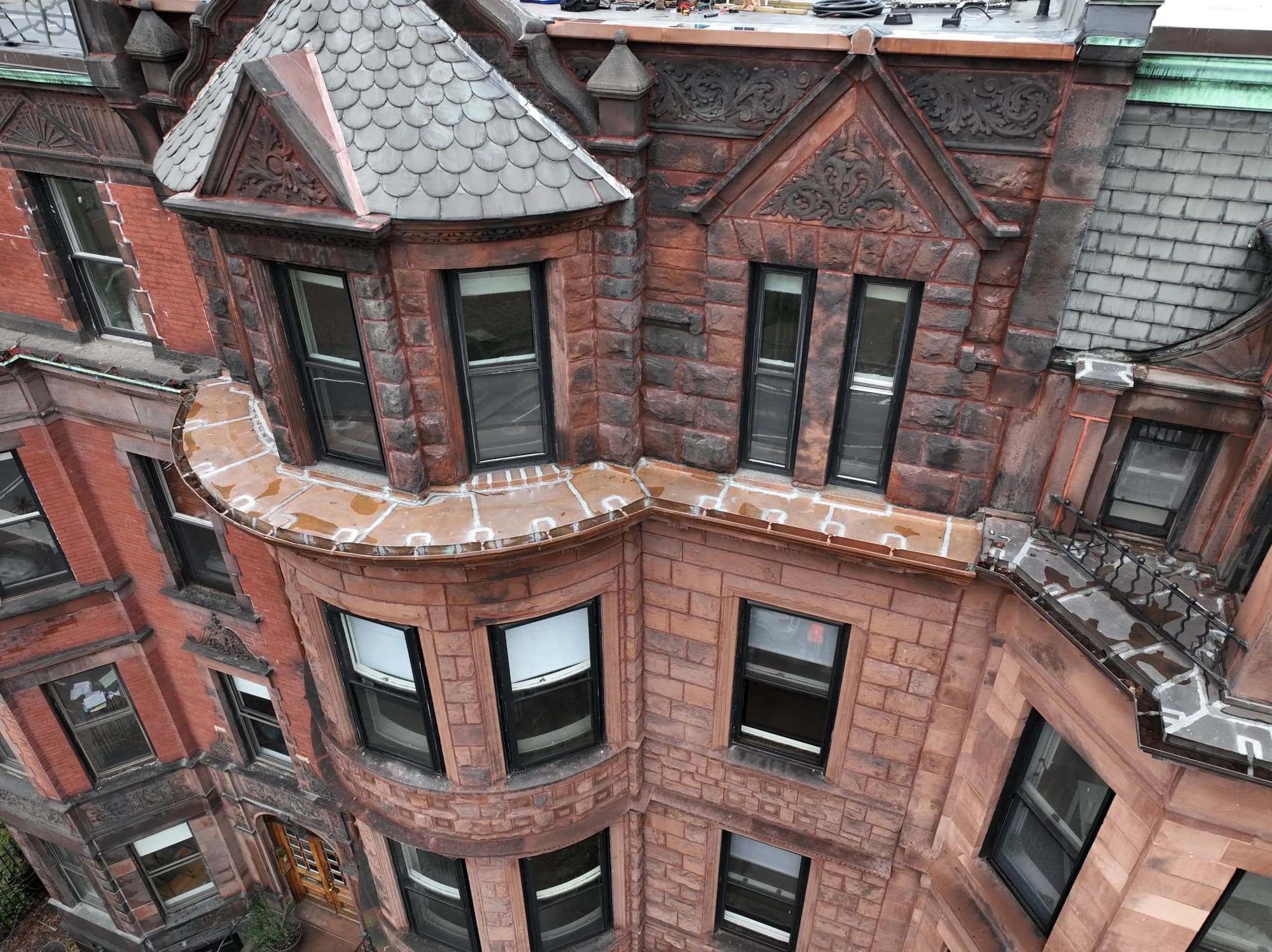 Aerial view of a historic Boston brownstone showing carved sandstone detailing, a slate turret roof, and copper flashing along the bay windows.