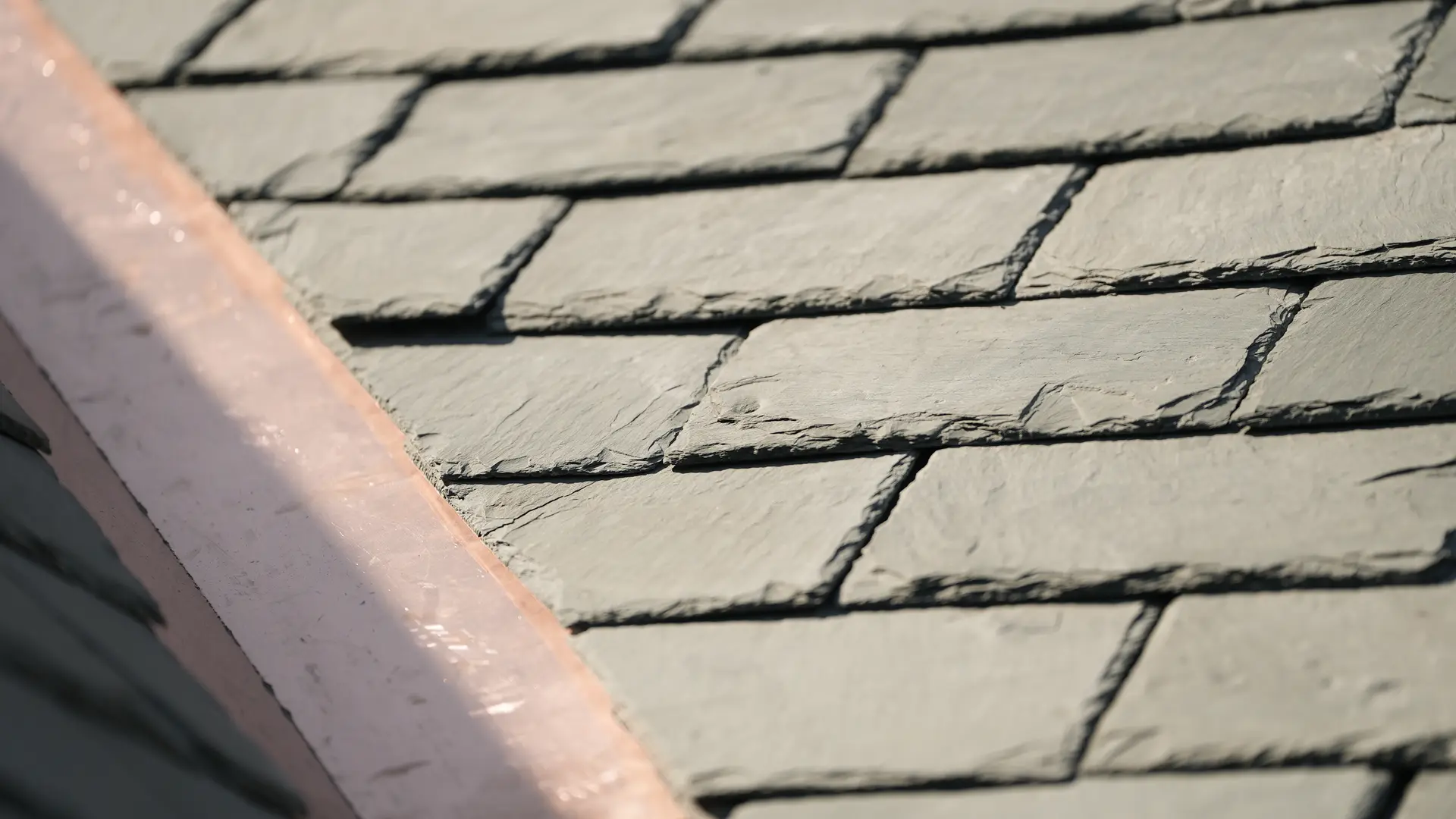 Close-up of newly laid slate courses with copper flashing on a historic roof.