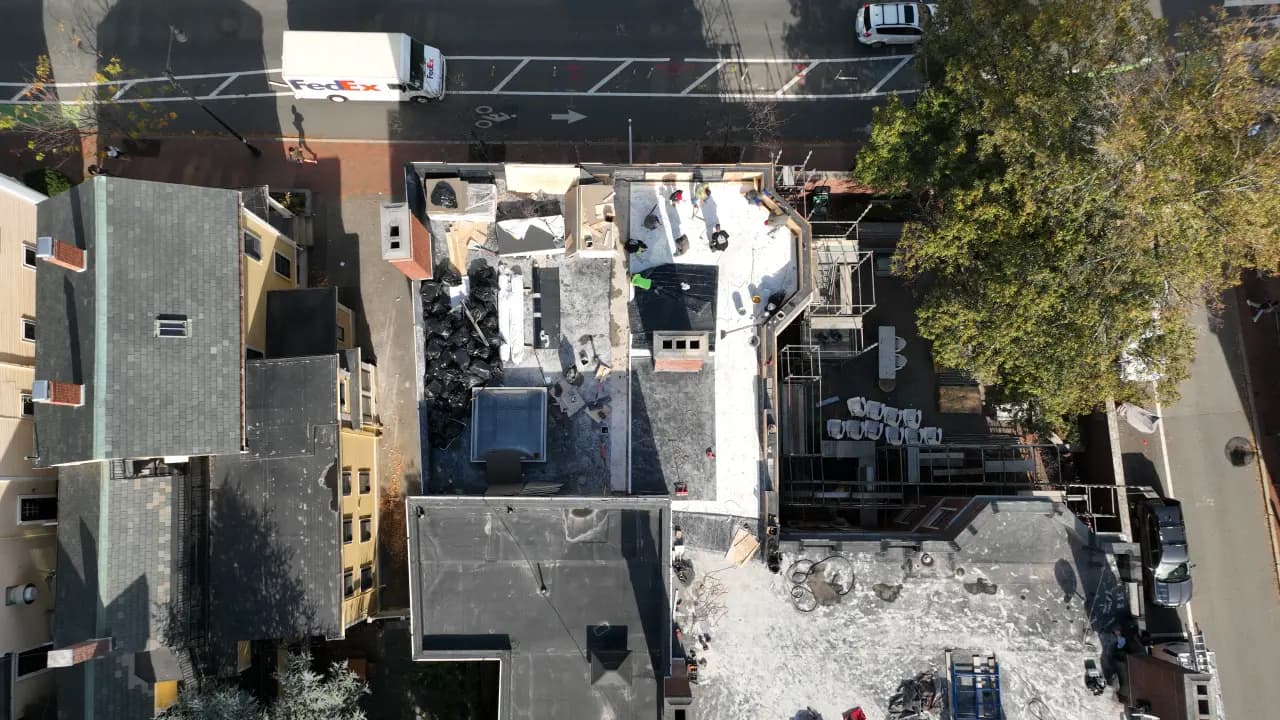 Aerial view of a commercial roof replacement in progress, with a city street and delivery truck below.