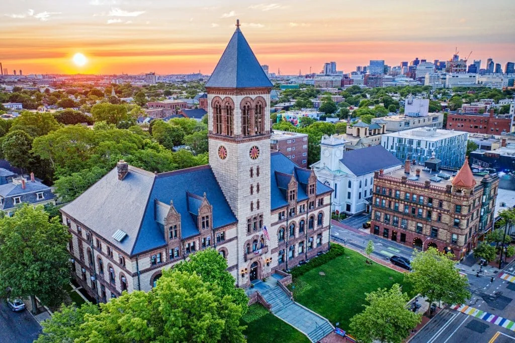 Aerial view of Cambridge City Hall at sunset with the Boston skyline beyond.