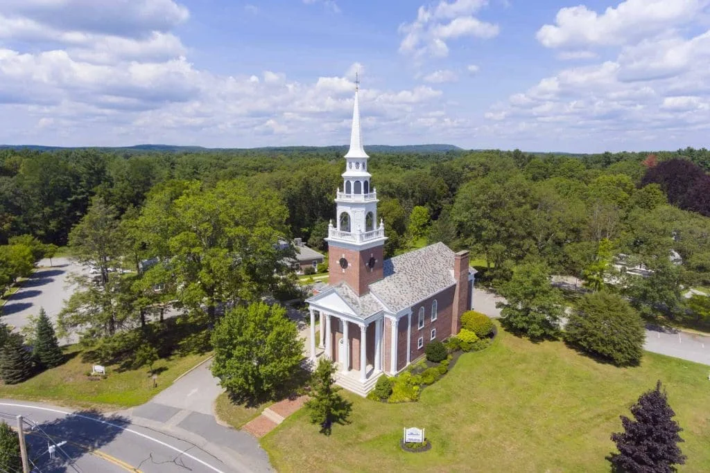 Aerial view of a steepled brick church among the trees in Framingham.