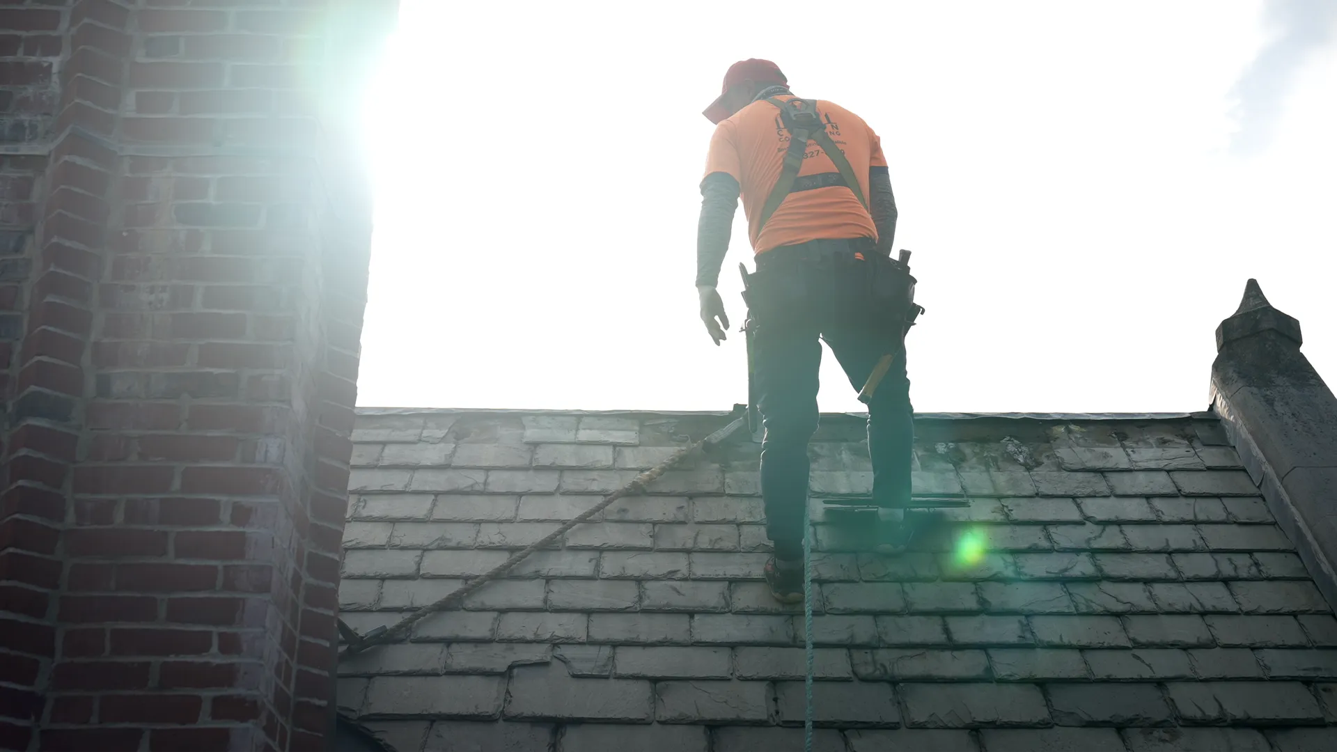 Silhouette of a roofer standing on a historic slate roof at golden hour.